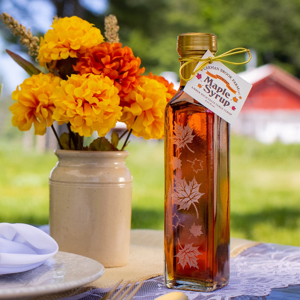 Autumn leaf maple syrup bottles displayed as wedding favor on table setting.